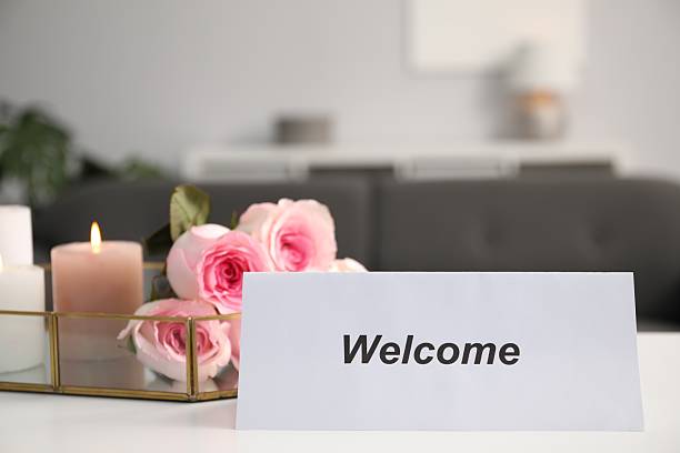 Card with word Welcome, roses and burning candles on white table. Space for text