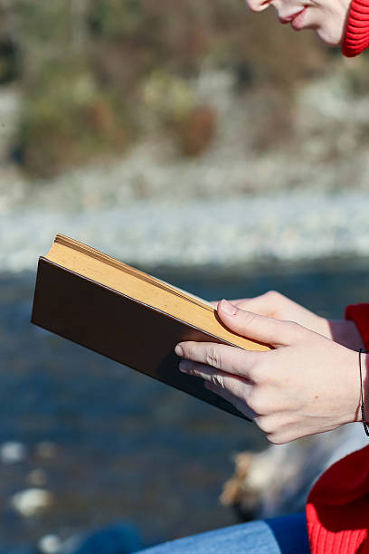 istock Partial face and hands with book by water 2248929823