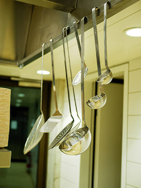 Hanging stainless steel ladles and kitchen utensils organized above cooking area in professional restaurant workspace with warm lighting and modern interior equipment