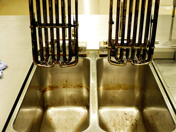 Used deep fryer heating elements placed above stainless steel basins with oil residue in professional restaurant kitchen after frying and before cleaning