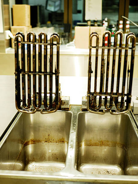 Used deep fryer heating elements placed above stainless steel basins with oil residue in professional restaurant kitchen after frying and before cleaning