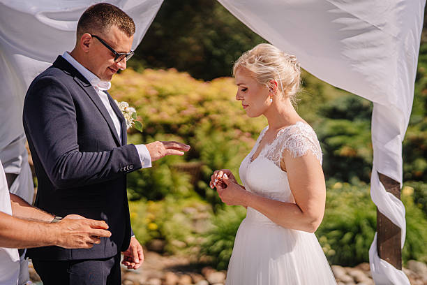 istock Bride and groom exchanging wedding rings during outdoor ceremony, surrounded by lush greenery and elegant drapery, capturing a moment of love and commitment in a beautiful setting 2248931457