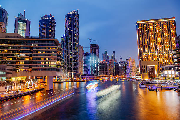 A vibrant evening view of Dubai Marina showcasing illuminated skyscrapers, luxury residential towers, and reflections shimmering on the water as boats move through the canal, highlighting the modern architecture and dynamic urban lifestyle in Dubai Marina United Arab Emirates