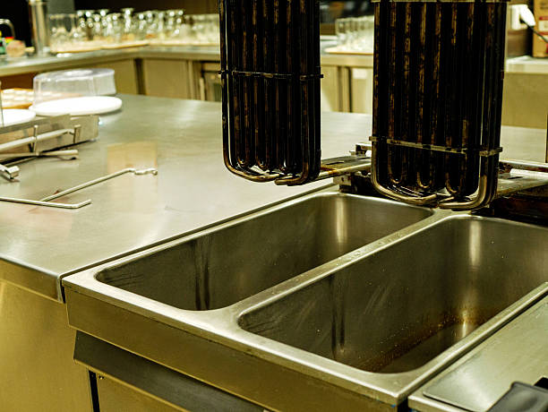 Stainless steel deep fryer basins in professional restaurant kitchen showing used dirty oil containers and cooking residue after frying process before cleaning