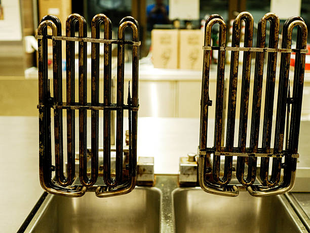 Used deep fryer heating elements placed above stainless steel basins with oil residue in professional restaurant kitchen after frying and before cleaning