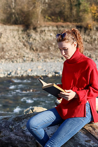 istock Woman on log reading book near stream 2248935922
