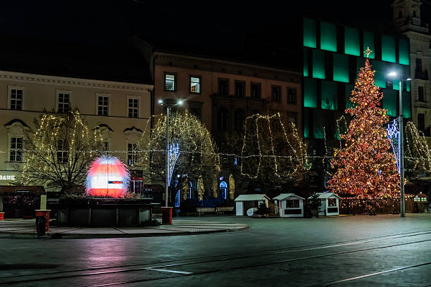 istock Nighttime city square illuminated with festive Christmas lights, featuring a brightly decorated Christmas tree at the center, surrounded by lit trees, buildings, and a quiet street. 2248941835