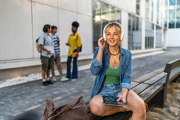 istock Smiling female student listening music on campus bench 2248946974