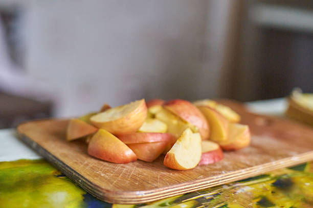 Freshly sliced red apples on wooden cutting board in a kitchen setting.