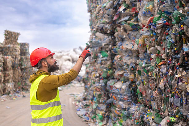 istock Side view of a worker in protective gear holding a digital tablet while checking bales of sorted plastic waste outdoors. Smart waste management and sustainable recycling process 2248948810