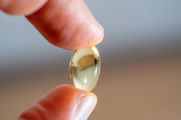 istock Omega-3 capsule tablet placed between the thumb and index finger. 2248950926