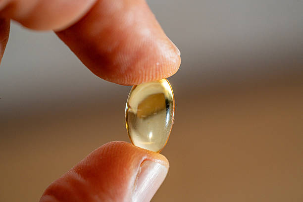 istock Omega-3 capsule tablet placed between the thumb and index finger. 2248950941