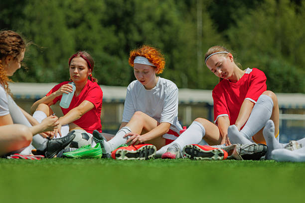 Teenagers participating in a girls' soccer training session, actively playing on a vibrant green artificial turf field with a coach overseeing the practice