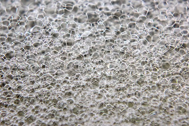 Bubbles create a captivating, textured surface with a hexagonal pattern, reflecting light beautifully. The close-up reveals the delicate structures and transparent qualities of the soap film.
