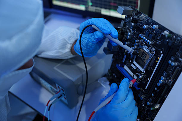 Engineers in sterile suits work at a semiconductor manufacturing plant using microscopes in a lab.