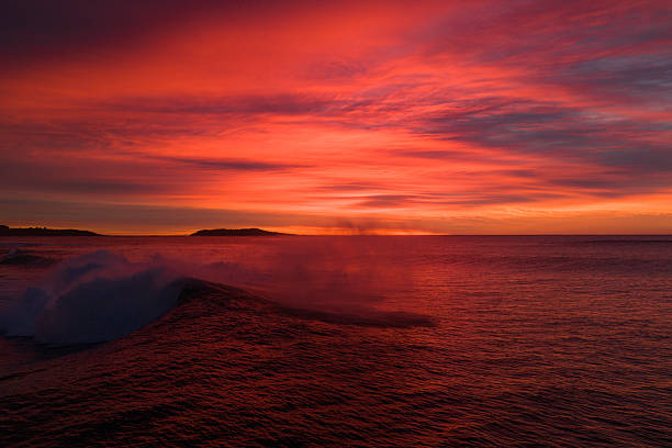 Vibrant red sunrise over ocean with breaking wave and dramatic sky — seascape, dawn surf, nature, coastal beauty, ocean horizon concept.