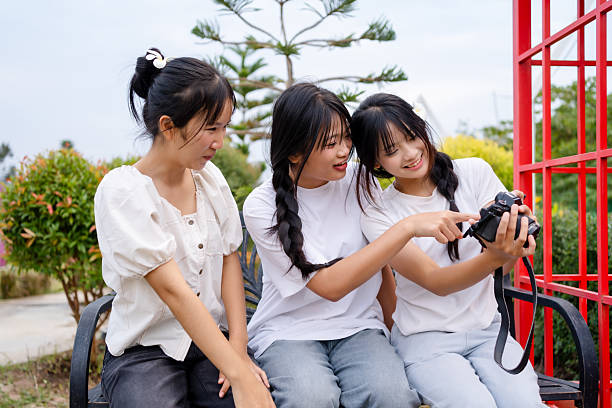 Three teenage friends reviewing photos on a camera outdoors. Real friendship, creativity, and joyful learning captured in a natural park setting.