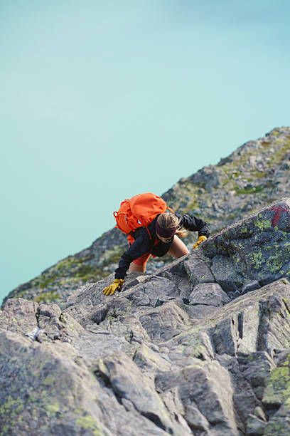 Young woman scrambles up mountain ridge above lake, Besseggen hike