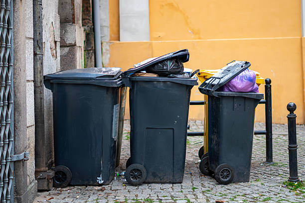 istock Overflowing waste bins standing by a yellow wall on a cobblestone courtyard in the middle of the city 2248978951