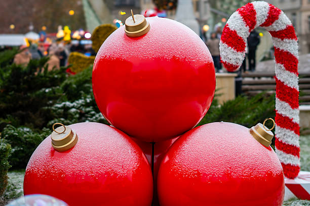 istock Christmas decorations with large red baubles covered in snow placed beside a red-white candy cane on a city square 2248978963