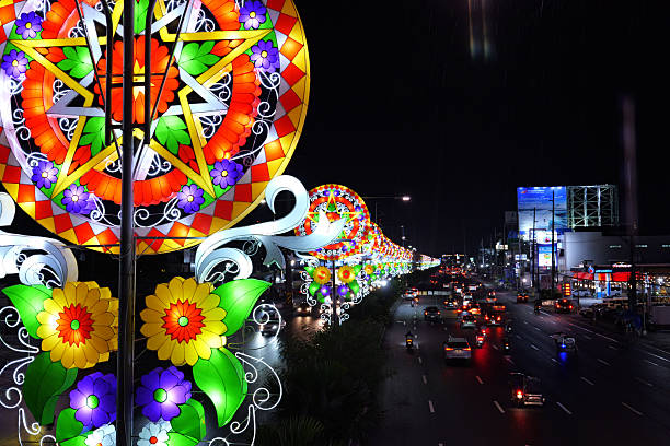 San Fernando, Pampanga Philippines - October 26, 2025: Nighttime scene featuring giant illuminated Christmas lanterns (parols) lining a busy highway in the Philippines. Bright, colorful star-shaped decorations glow above moving traffic, with reflections on the wet road and city lights in the background.