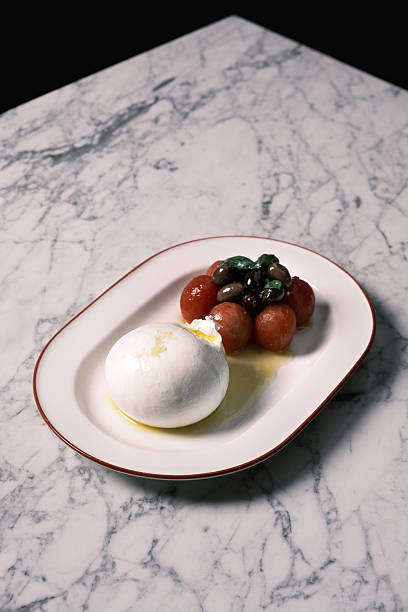 Top view of fresh buffalo burrata served with marinated cherry tomatoes and mixed olives on a white oval plate, Classic Italian restaurant presentation from Italy, Culinary styling concept for menu design and food branding