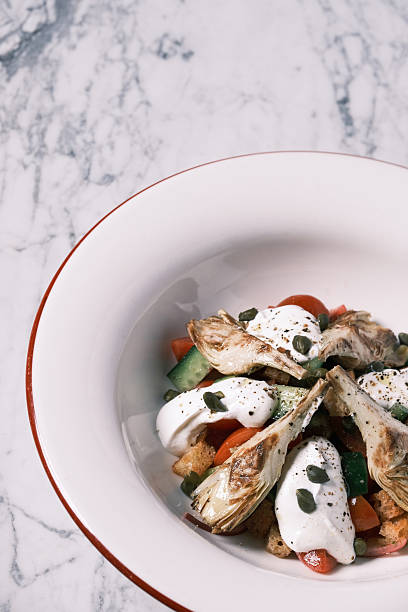 View of fresh artichoke hearts served over a mixed vegetable salad with creamy dressing, Contemporary Italian restaurant presentation inspired by Mediterranean produce, Culinary concept for menu design and food branding