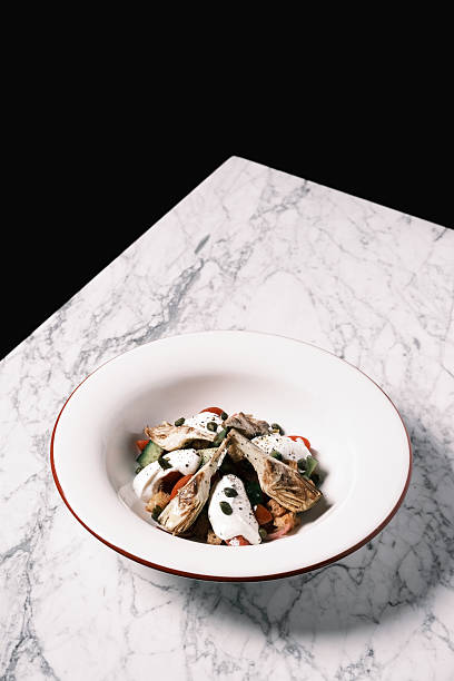 View of fresh artichoke hearts served over a mixed vegetable salad with creamy dressing, Contemporary Italian restaurant presentation inspired by Mediterranean produce, Culinary concept for menu design and food branding