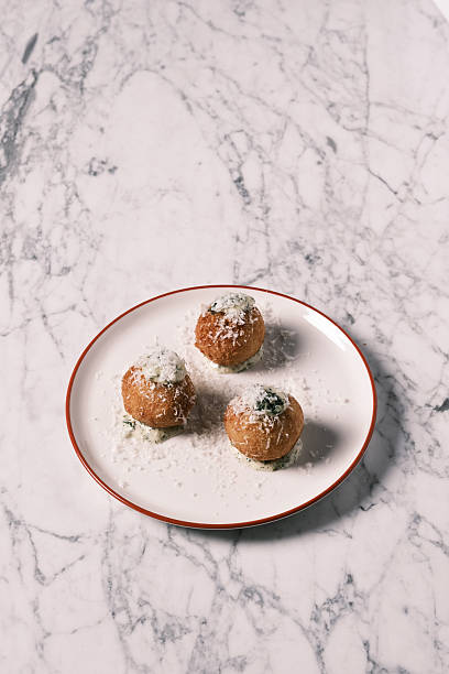 High angle view of Italian arancini served with creamy herb sauce and grated cheese on a white plate, Traditional Sicilian rice balls reimagined in contemporary restaurant style, Gourmet appetizer concept for menu design and food branding