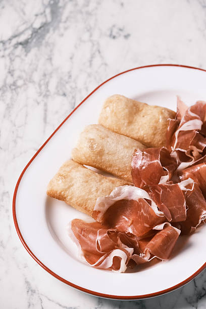 High angle view of Prosciutto Crudo served with warm fried gnocco on a white plate, Traditional Northern Italian antipasto from Emilia-Romagna, Gourmet serving concept for restaurant menu and culinary presentation