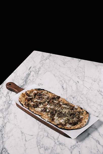 View of lamb pancetta pizzetta with mozzarella and herbs on wooden board, Modern Italian flatbread topped with slow-cooked lamb and aromatic seasoning, Gourmet restaurant concept for fine dining menu and culinary design