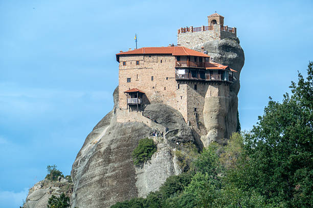 A stunning view of Meteora's rock formations with a monastery perched atop, under a clear sky in Greece.