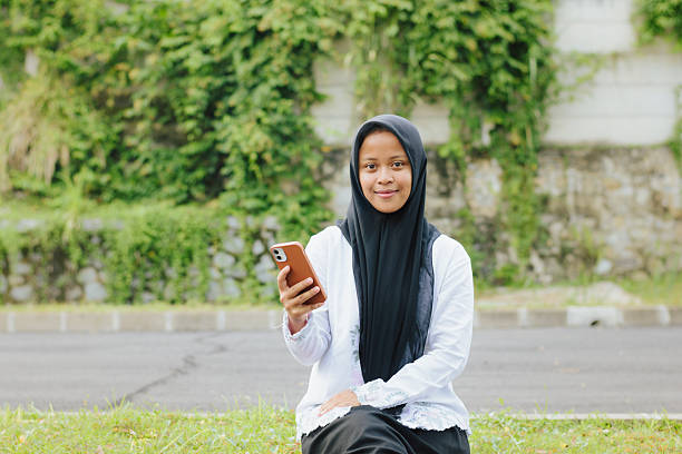 istock Confident Indonesian Muslim Student Holding Smartphone and Smiling at Camera 2248984875