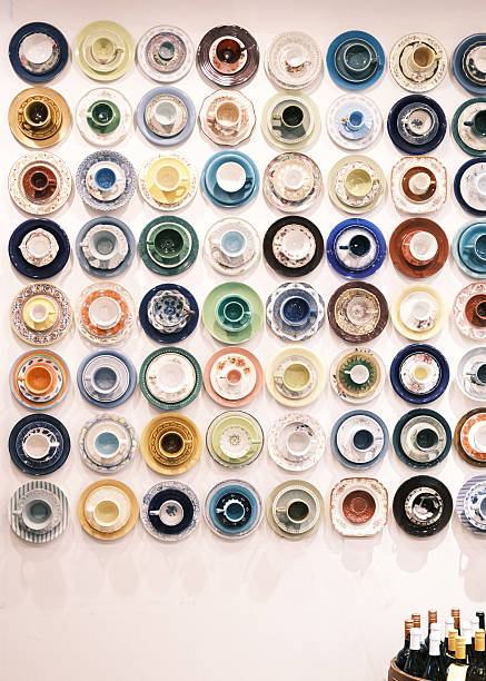 This image presents a vibrant wall installation composed of numerous Turkish coffee cups and saucers arranged in a structured grid. Each set features unique colors, patterns and ceramic styles, highlighting the richness of regional craftsmanship and cultural aesthetics. The clean background enhances the visual rhythm created by the repetition of circular forms, making the composition suitable for themes related to Turkish coffee culture, interior decoration, hospitality branding, design inspiration and cultural heritage displays.