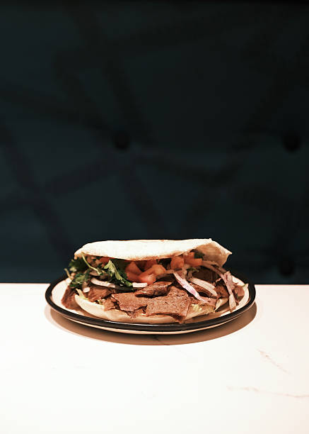 Front view of a Turkish-style meat sandwich made with sliced beef, tomatoes, onions and herbs served in soft flatbread on a plate, Traditional street food presentation reflecting authentic dining culture for menu and promotional design.
