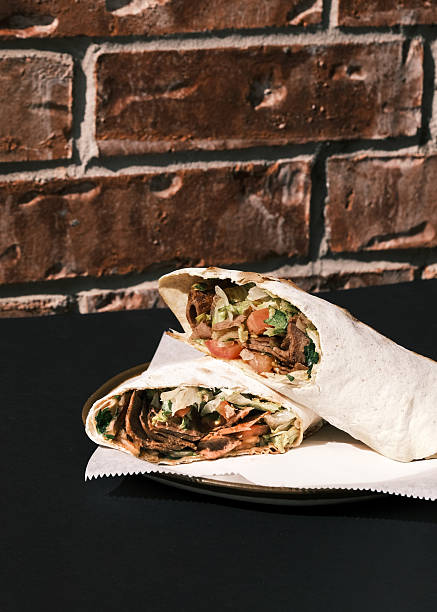 Close-up view of a sliced Turkish meat wrap filled with grilled beef, lettuce and tomatoes on a plate in a restaurant setting, Traditional street food presentation and culinary concept suitable for menu design and promotional materials.
