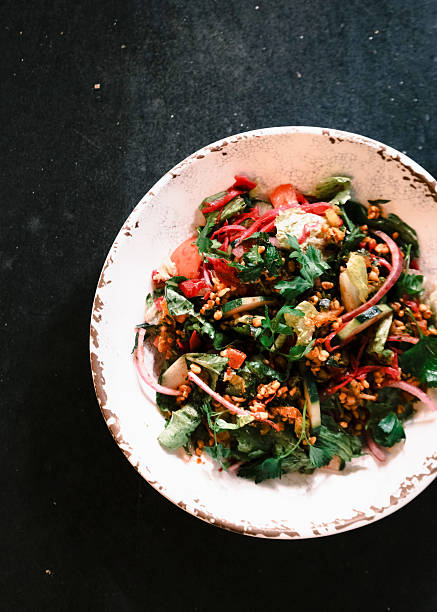 Top view of a vibrant Turkish-style mixed salad with fresh greens, tomatoes, onions, herbs and crunchy grains served in a rustic ceramic bowl, Mediterranean healthy food concept presented on a dark surface for culinary design and menu visuals