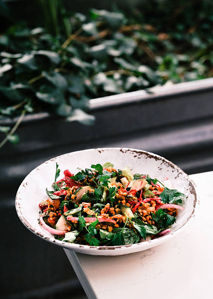Top view of a vibrant Turkish-style mixed salad with fresh greens, tomatoes, onions, herbs and crunchy grains served in a rustic ceramic bowl, Mediterranean healthy food concept presented on a dark surface for culinary design and menu visuals