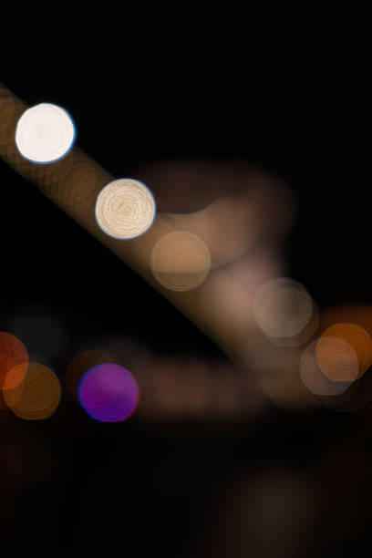 Budapest, Hungary - April 2025 This is a defocused image of the historic Széchenyi Chain Bridge, a suspension bridge connecting Buda and Pest in Budapest, Hungary, viewed at night. The bridge's lights are shown as Bokeh circles along its cables and towers, creating a striking silhouette against the dark sky. The scene includes distant city lights on both riverbanks, suggesting urban activity without visible crowds. This night time urban landscape conveys a sense of peace and tranquillity, ideal for backgrounds and commercial uses such as travel brochures promoting European destinations, articles on Hungarian history, tourism websites featuring Budapest landmarks, book covers for city guides, or editorial content on iconic bridges worldwide. The composition is of the bridge's 19th-century design by William Tierney Clark, with no people present, focusing on the illuminated structure and watery foreground.