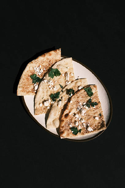 Top view of traditional Turkish flatbread slices topped with crumbled white cheese and parsley, Rustic Mediterranean presentation on a white background, Culinary culture and bakery concept for menu and branding design