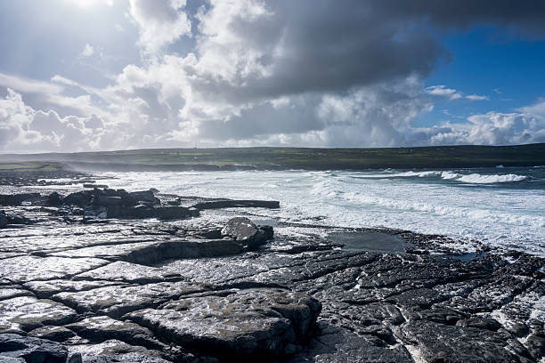 Doolin Pier in Ireland. A rocky landscape under a blue sky with clouds. In the background the Atlantic ocean.