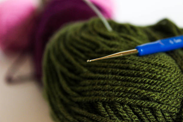 Blue-handled 0.5 mm steel crochet hook resting on an olive yarn ball. Concept of precision lacework and delicate crafting tools.