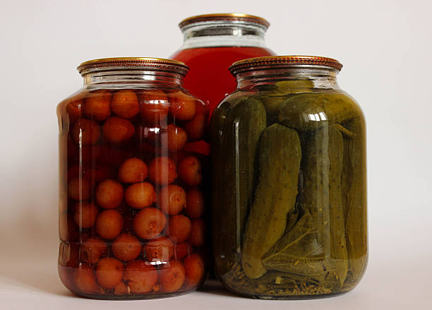 Three large glass jars. fruit compote, pickled cucumbers, and another compote on a white background.