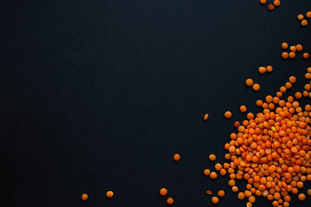Uncooked red lentils scattered across a black textured surface, leaving generous copy space. Minimal flat lay for diet, vegan protein or recipe themes.