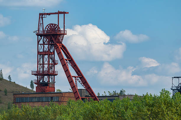Red mine headframe structure against a blue sky with green trees in foreground