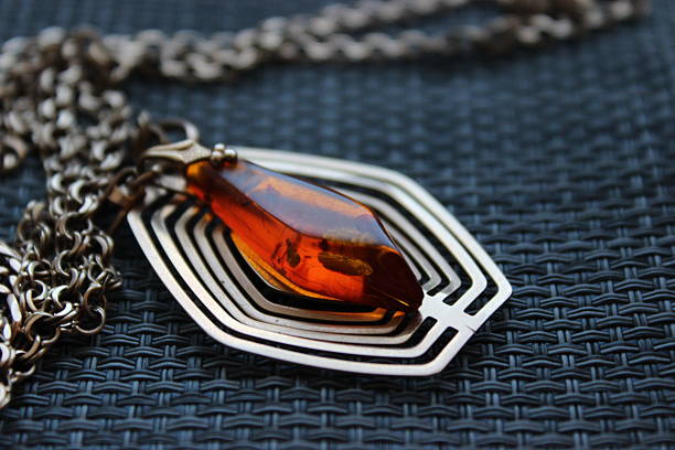 Artistic still life of an amber pendant placed over a layered geometric metal frame on dark textured background - graphic, modern composition.