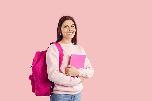 istock Happy university student girl with books and backpack standing isolated on pink background 2249015761