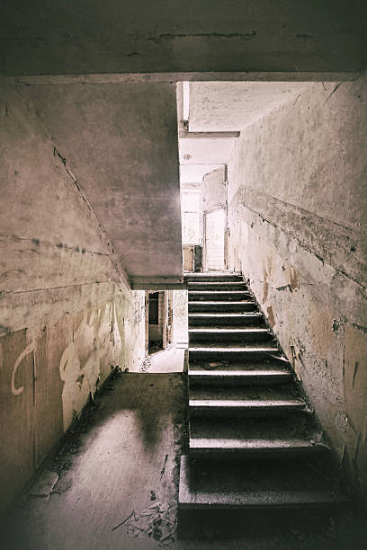 istock Grungy staircase shot in abandoned concrete building lit by dim window light through upper doorway 2249016589