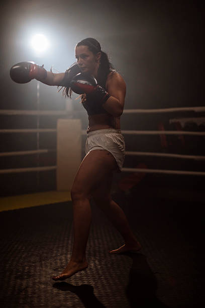 istock Female boxer throws powerful punch in dim boxing ring 2249017917