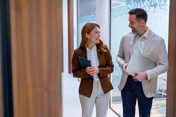istock Business professionals walking in modern office corridor, discussing work, holding tablet and laptop 2249022463